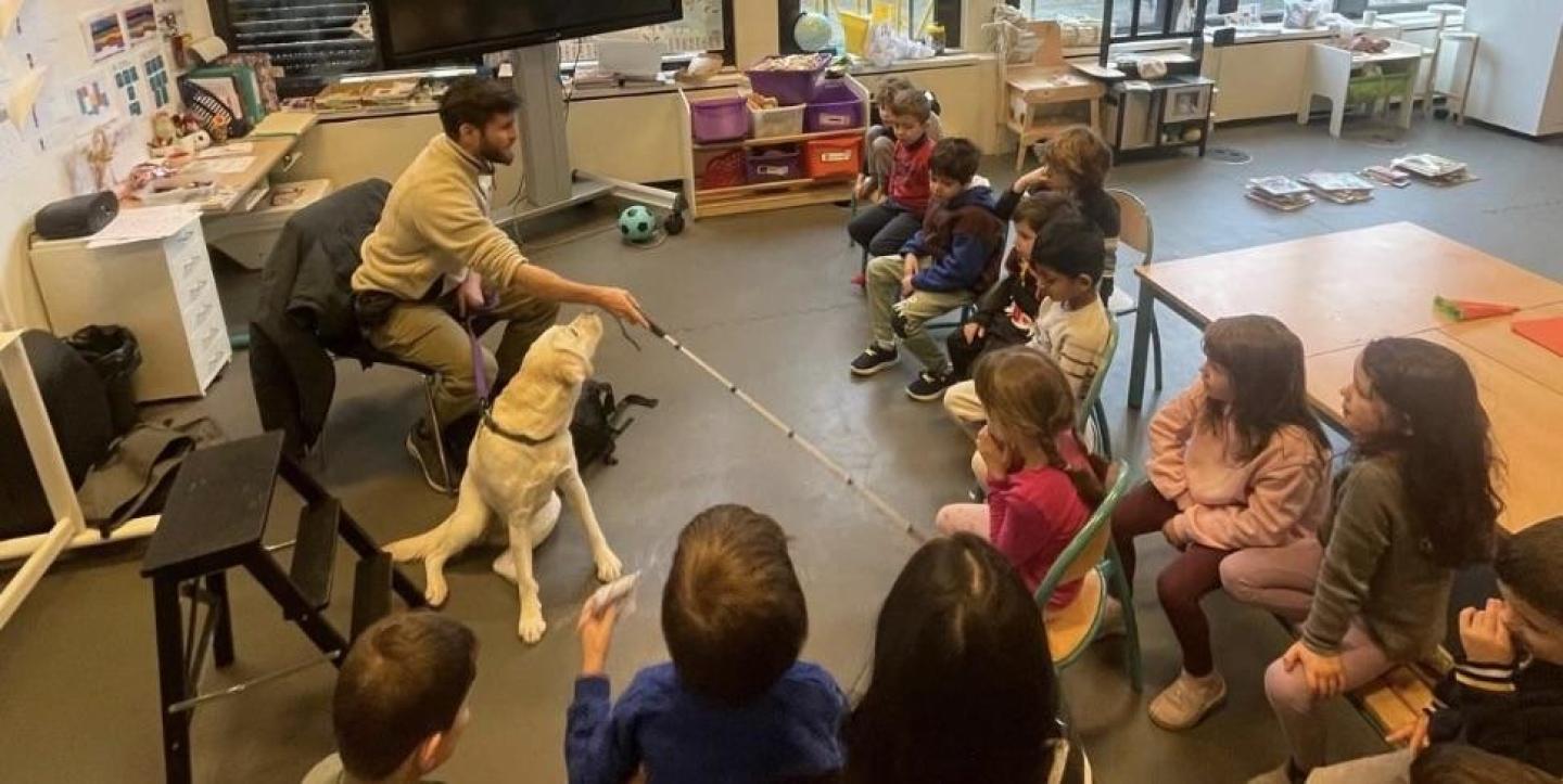 Cercle d'enfants autour d'un chien guide et une personne aveugle