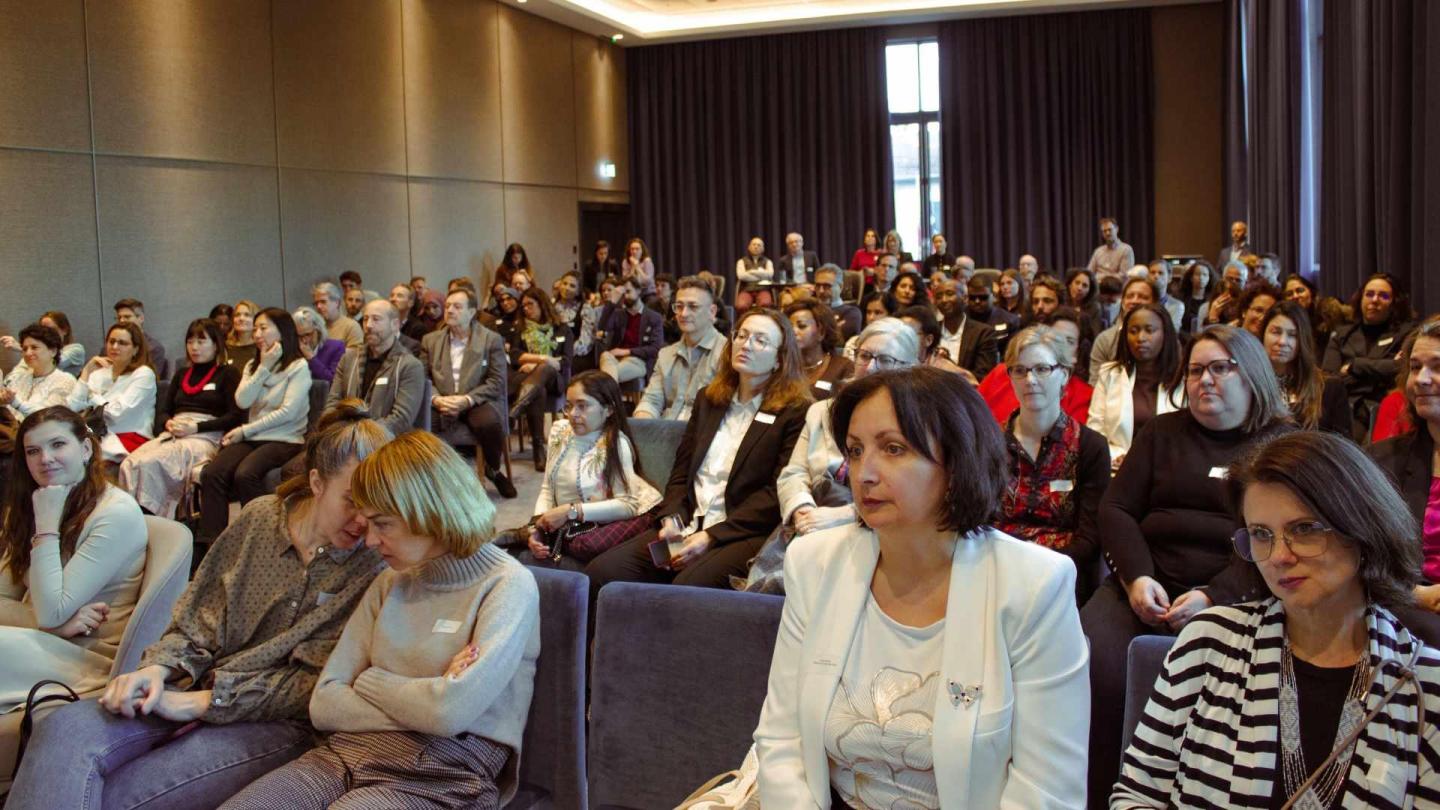 Salle avec une centaine de participants écoutant les témoignages